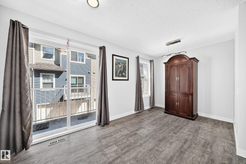 Spacious room with wood-finish flooring, white walls, and a prominent sliding glass door - 146 5604 199 Street, Edmonton, AB 