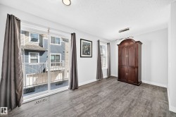 Spacious room with wood-finish flooring, white walls, and a prominent sliding glass door - 