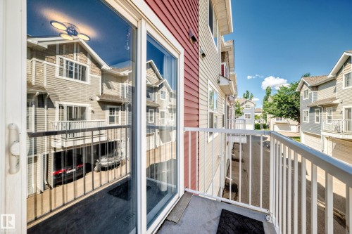 Private balcony with white metal railing, red and beige siding, sliding glass door, and exterior lighting fixture - 146 5604 199 Street, Edmonton, AB 