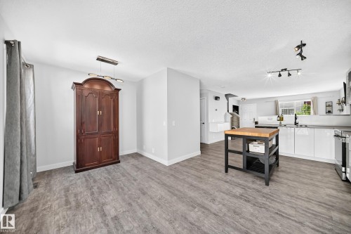 Open-concept living space featuring wood-finish flooring, a modern linear chandelier, recessed lighting, and track lighting - 146 5604 199 Street, Edmonton, AB 