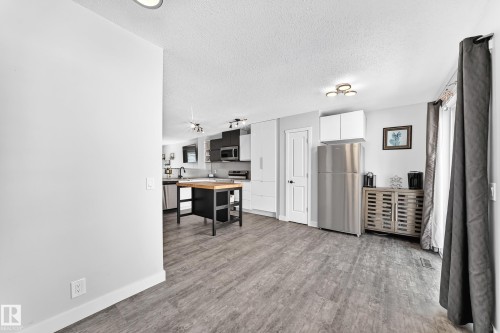 Open-concept living area featuring wood-finish flooring, a contemporary kitchen with stainless steel appliances, white and gray cabinetry, and a central island with a wood countertop - 146 5604 199 Street, Edmonton, AB 
