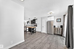 Open-concept living area featuring wood-finish flooring, a contemporary kitchen with stainless steel appliances, white and gray cabinetry, and a central island with a wood countertop - 