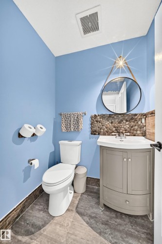 Half bath featuring a corner vanity with integrated sink, pebble stone backsplash, circular mirror, and tile flooring - 146 5604 199 Street, Edmonton, AB 