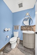 Half bath featuring a corner vanity with integrated sink, pebble stone backsplash, circular mirror, and tile flooring - 