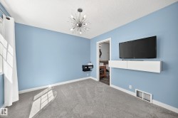 Carpeted room featuring a contemporary sputnik chandelier, light blue painted walls, a built-in white floating media console, and a window with white sheers - 