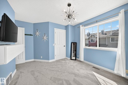 Spacious room with light blue walls, gray carpeting, and a modern sputnik-style chandelier - 146 5604 199 Street, Edmonton, AB 