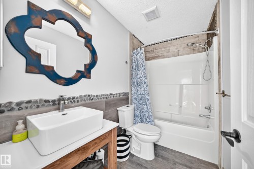 Bathroom featuring a vessel sink on a wood-finish vanity, decorative mirror, and a full bathtub with a shower - 146 5604 199 Street, Edmonton, AB 