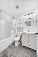 White bathroom featuring a single vanity with light wood-finish cabinetry, a white countertop, and a round black-framed mirror - 