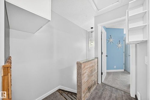 Hallway featuring wood-finish flooring, a stone-accented half-wall, and a contemporary pendant light fixture - 146 5604 199 Street, Edmonton, AB 