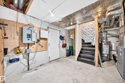 Utility area featuring a concrete floor, exposed ceiling joists, electrical panel, water heater, and an adjacent staircase with textured paneling - 