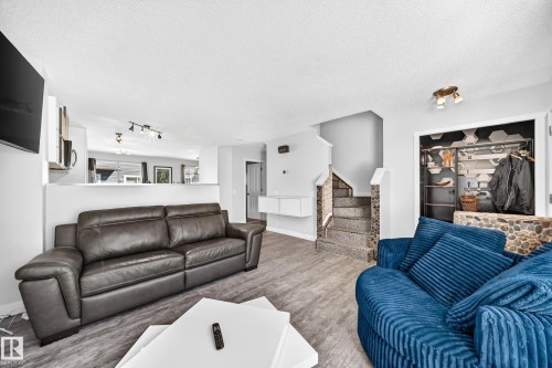 Living area featuring wood-finish flooring, a contemporary staircase with stone-clad risers, a built-in shelving unit, and a pass-through to a background space - 146 5604 199 Street, Edmonton, AB 