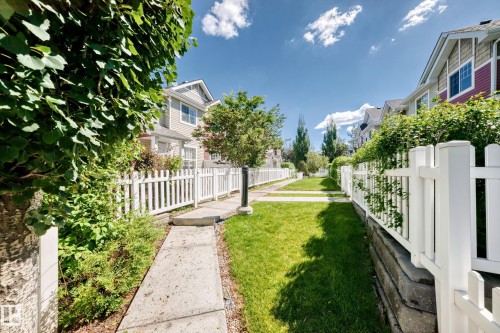 Concrete pathway bordered by a white picket fence and lush green landscaping - 146 5604 199 Street, Edmonton, AB 