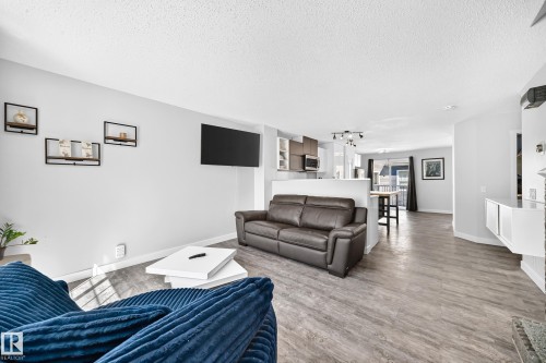 Open-concept living area featuring wood-finish flooring, a contemporary entertainment wall with shelving, and a clear sightline to the kitchen and dining areas - 146 5604 199 Street, Edmonton, AB 