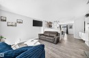 Open-concept living area featuring wood-finish flooring, a contemporary entertainment wall with shelving, and a clear sightline to the kitchen and dining areas - 146 5604 199 Street, Edmonton, AB 
