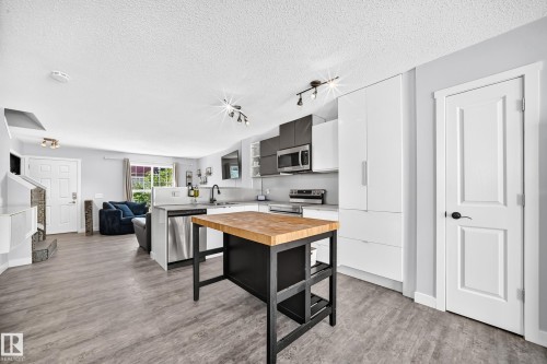 Contemporary kitchen featuring a butcher block island, stainless steel appliances, white flat-panel cabinetry, and wood-finish flooring - 146 5604 199 Street, Edmonton, AB 