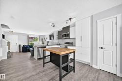 Contemporary kitchen featuring a butcher block island, stainless steel appliances, white flat-panel cabinetry, and wood-finish flooring - 