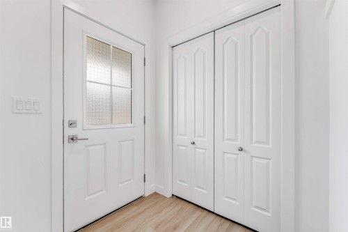 Entryway featuring a paneled door with frosted glass, brushed nickel hardware, light wood-finish flooring, and two sets of bifold closet doors - 1208 14 Ave Nw, Edmonton, AB 