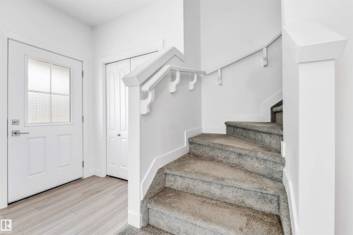 Entryway featuring a white paneled door with textured glass, wood-finish flooring, a white bi-fold closet, and a carpeted staircase with a white handrail - 1208 14 Ave Nw, Edmonton, AB 