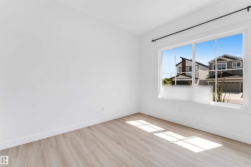 Bright room featuring a large multi-pane window, light wood-finish flooring, white baseboards, and a black curtain rod - 1208 14 Ave Nw, Edmonton, AB 