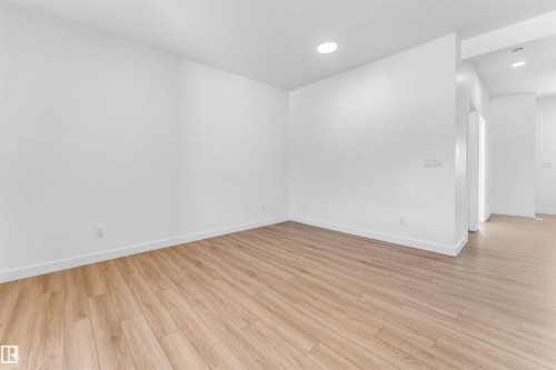 Spacious interior featuring light wood-finish flooring, white baseboards, and recessed ceiling lighting - 1208 14 Ave Nw, Edmonton, AB 