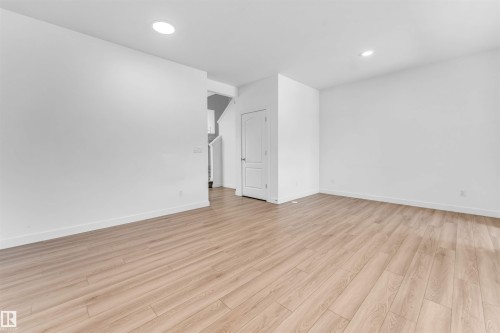 Spacious room featuring light wood-finish flooring, white baseboards, recessed ceiling lighting, and a white interior door - 1208 14 Ave Nw, Edmonton, AB 