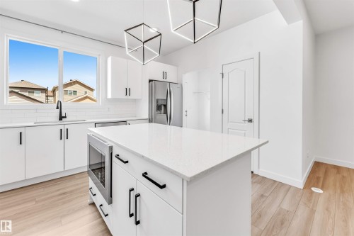 Modern kitchen featuring a central island with integrated microwave, white cabinetry, quartz countertops, stainless steel appliances, and wood-finish flooring - 1208 14 Ave Nw, Edmonton, AB 