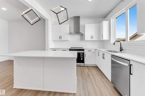 Kitchen featuring a large central island, white cabinetry, stainless steel appliances, and wood-finish flooring - 1208 14 Ave Nw, Edmonton, AB 