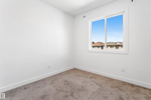 Bright interior room featuring a large window with white trim, plush carpet flooring, white painted walls, and white baseboards - 1208 14 Ave Nw, Edmonton, AB 