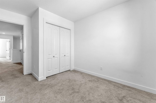Carpeted room featuring a double bifold closet door with arched paneling, white baseboards, and neutral wall paint - 1208 14 Ave Nw, Edmonton, AB 