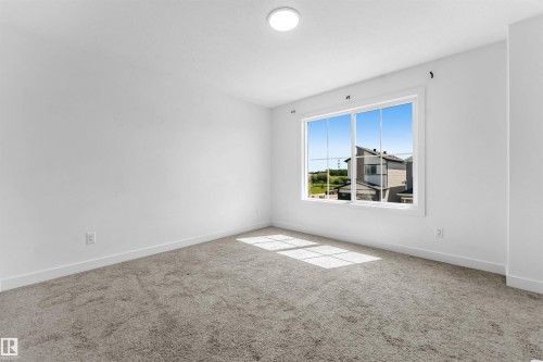 Bright room featuring a large window with white trim, gray carpet, white walls, and a ceiling-mounted light fixture - 1208 14 Ave Nw, Edmonton, AB 