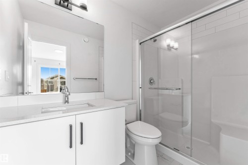 Modern bathroom featuring a glass-enclosed shower with a built-in bench, a white vanity with an integrated sink, and a large wall-mounted mirror - 1208 14 Ave Nw, Edmonton, AB 
