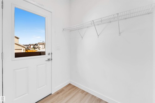 Entryway featuring a white paneled door with an upper glass insert, wood-finish flooring, white walls, and a white wire shelving system - 1208 14 Ave Nw, Edmonton, AB 