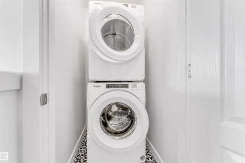 Dedicated laundry area featuring a stacked white front-loading washer and dryer, patterned floor tile, and bright white walls - 1208 14 Ave Nw, Edmonton, AB 