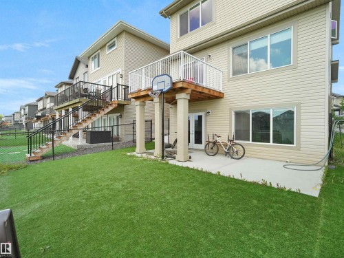Rear exterior featuring beige siding, an upper deck with white railings, a ground-level patio, and an artificial turf lawn - 4615 175 Avenue, Edmonton, AB 