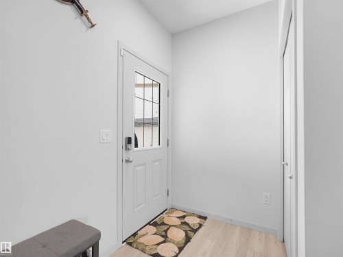 Entryway with a white paneled door featuring a window with grilles, light wood-finish flooring, and a built-in closet with white bifold doors - 4615 175 Avenue, Edmonton, AB 
