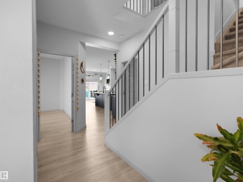 Entryway featuring wood-finish flooring extending into the kitchen, a contemporary staircase with dark balusters, recessed lighting, and a white interior color palette - 4615 175 Avenue, Edmonton, AB 