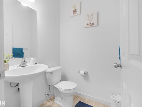 Pedestal sink with a polished chrome faucet, rectangular mirror, and light wood-finish flooring - 4615 175 Avenue, Edmonton, AB 