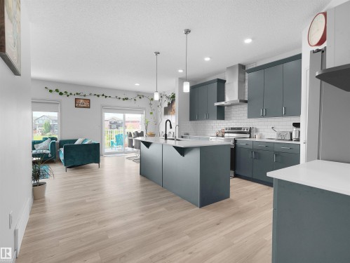 Open-concept kitchen featuring an island with a breakfast bar, white countertops, a subway tile backsplash, and a stainless steel appliance suite including a range with an overhead vent hood - 4615 175 Avenue, Edmonton, AB 