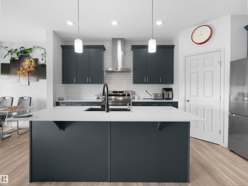 Kitchen featuring a large central island with a white countertop, dark cabinetry, subway tile backsplash, stainless steel appliances, and wood-finish flooring - 4615 175 Avenue, Edmonton, AB 