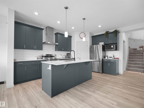 Modern kitchen featuring wood-finish flooring, a central island with a white countertop, and pendant lighting - 4615 175 Avenue, Edmonton, AB 