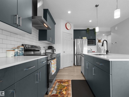 Kitchen featuring dark teal cabinetry, white countertops, subway tile backsplash, and stainless steel appliances including a refrigerator and range - 4615 175 Avenue, Edmonton, AB 