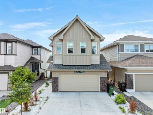 Modern two-story residence featuring light beige vertical and horizontal siding, a prominent front-facing gable, and stone veneer accents - 4615 175 Avenue, Edmonton, AB 