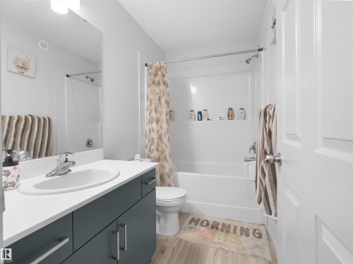 Bathroom featuring a white bathtub with an integrated shower, a vanity with a white countertop and dark gray cabinetry, a large wall-mounted mirror, and wood-finish flooring - 4615 175 Avenue, Edmonton, AB 