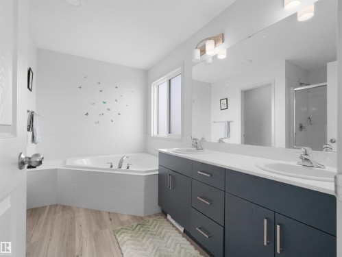 Bathroom featuring a corner soaking tub, dual vanity with undermount sinks, and light wood-finish flooring - 4615 175 Avenue, Edmonton, AB 