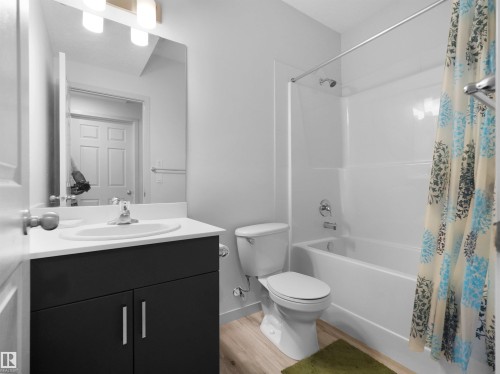 Bathroom featuring a white vanity countertop with an integrated sink, dark wood-finish cabinetry, chrome fixtures, and a white bathtub with a shower - 4615 175 Avenue, Edmonton, AB 