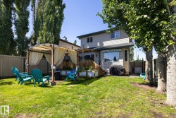 Expansive backyard featuring a gazebo with fabric curtains, a multi-level wooden deck, and a window with a striped awning - 