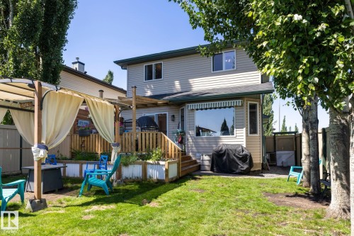 Expansive backyard featuring a manicured lawn, a two-story home with light-colored siding, a multi-level wooden deck, and mature trees providing natural screening - 60 Leyland Way, Spruce Grove, AB 