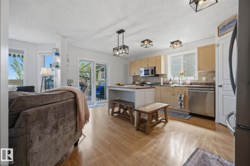 Open-concept kitchen featuring wood-finish flooring, light wood cabinetry, stainless steel appliances, and a central island with a contrasting countertop - 60 Leyland Way, Spruce Grove, AB 