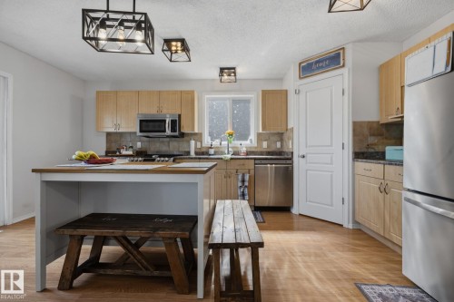 Kitchen featuring ample light wood cabinetry, stainless steel appliances, wood-finish flooring, a tile backsplash, and a central island with countertop space - 60 Leyland Way, Spruce Grove, AB 