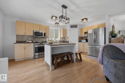 Bright kitchen featuring light wood cabinetry, dark countertops, stainless steel appliances, a center island, and wood-finish flooring - 